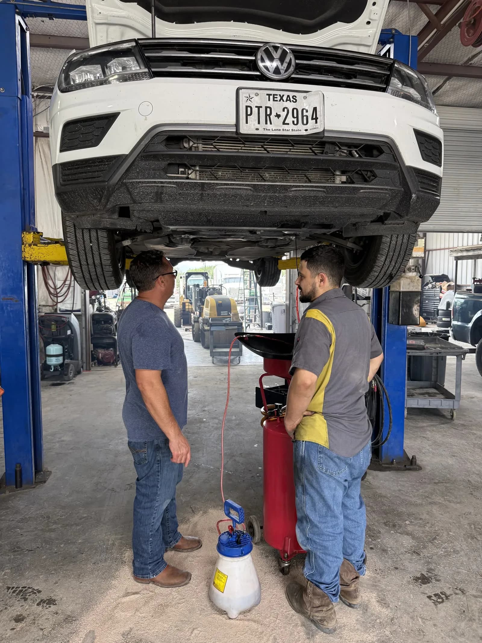 Quality Mechanics technicians working under a pickup on a two-post lift