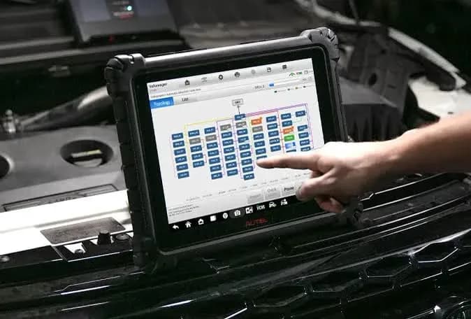 Technician using an Autel diagnostic tablet showing the vehicle module topology map
