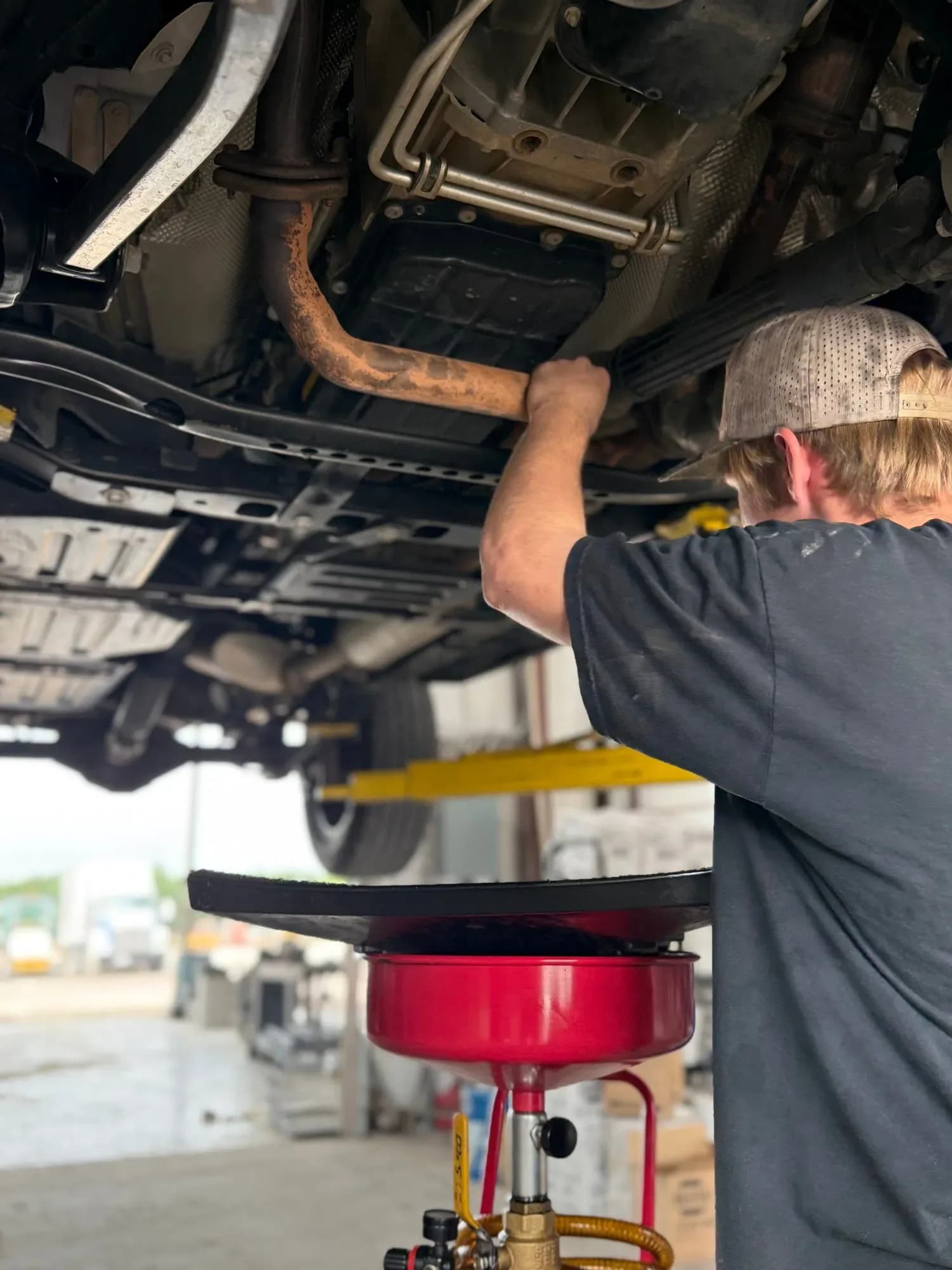 Quality Mechanics technician performing an oil change under a lifted vehicle