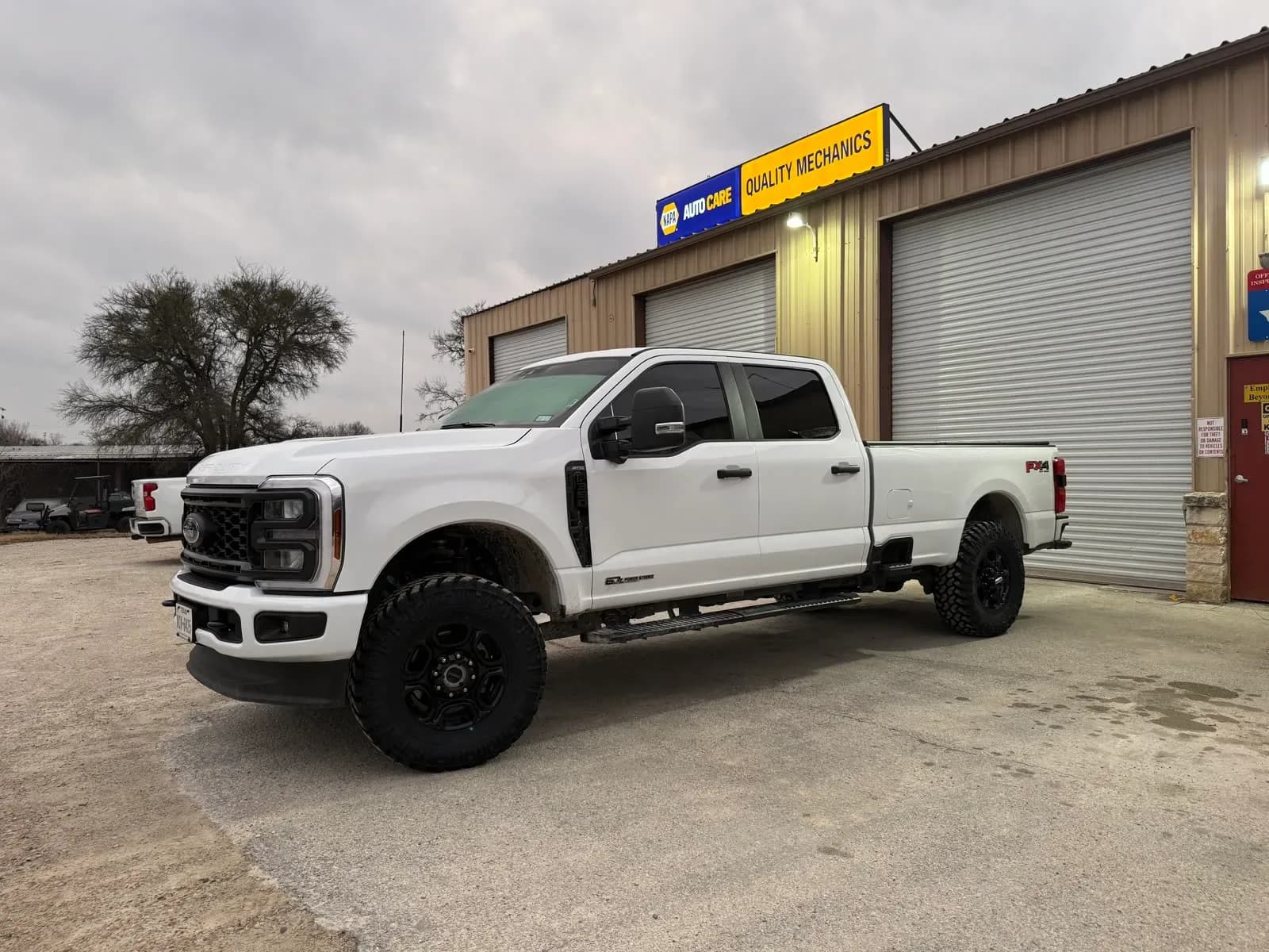 Leveled white Ford F-250 FX4 on off-road tires in front of the Quality Mechanics shop in Waco